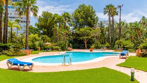 Piscina com espreguiçadeiras, cercada por gramado bem cuidado e palmeiras.