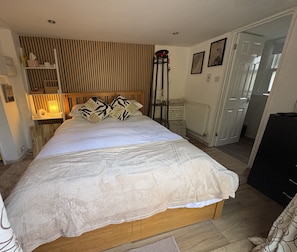 Ein Schlafzimmer mit Holz-Kopfteil, einem Bett mit weißen Bettbezügen, einem Heizkörper, einer Tür und einer Wand mit vertikalen Jalousien.