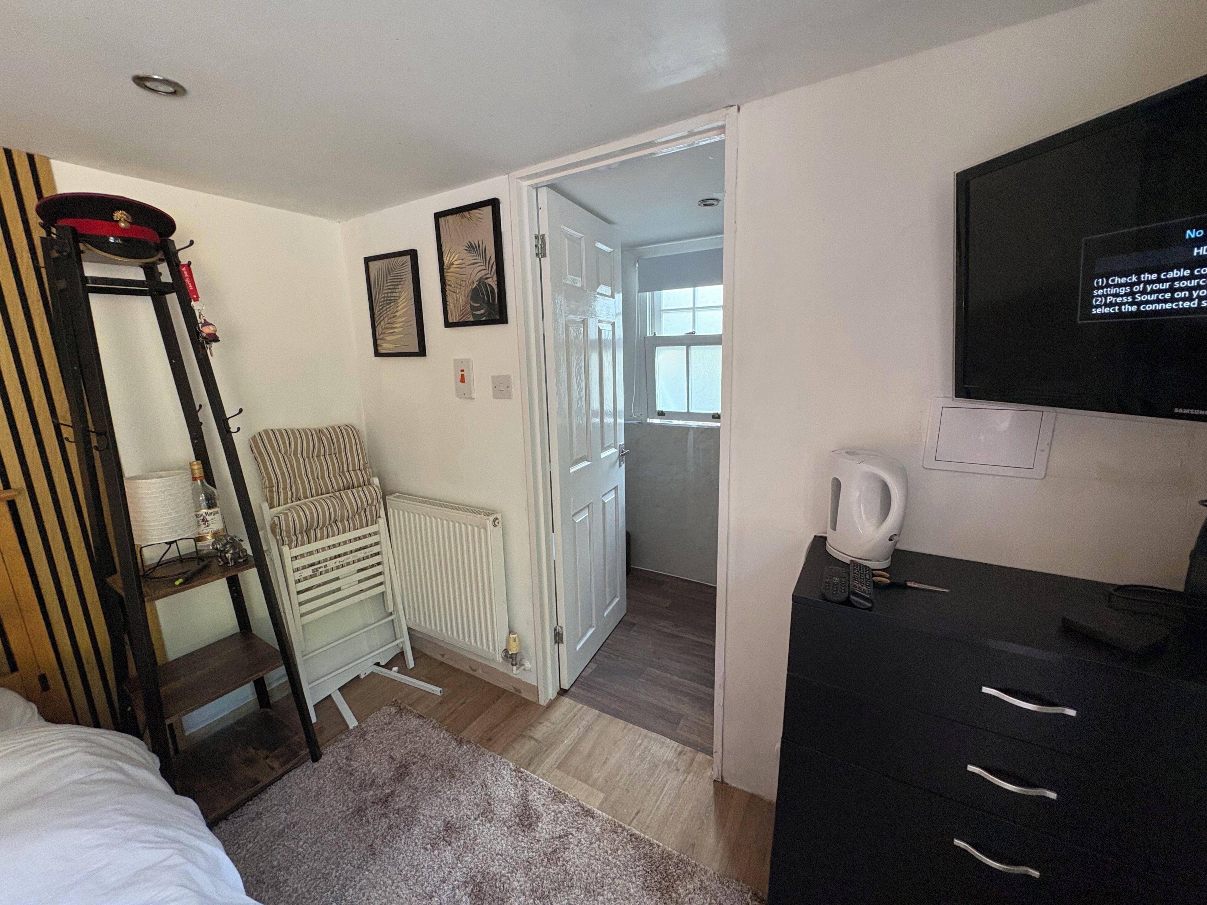 Un dormitorio con una cama, un radiador, una silla, un televisor y un hervidor.