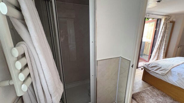 Een slaapkamer met een bed, douche en badkamer met handdoekrek.