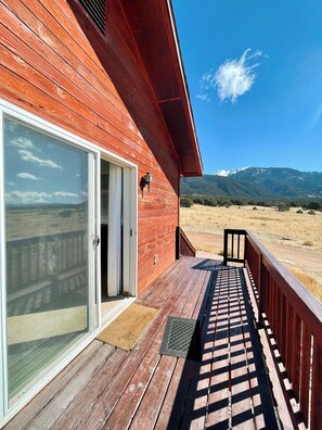 A wooden building with a deck, a sliding glass door, and a view of mountains. - Family Ranch house with Mountain View’s (Crestone)