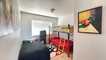 Une chambre avec des lits superposés, une télévision, un bureau et une fenêtre avec des stores.