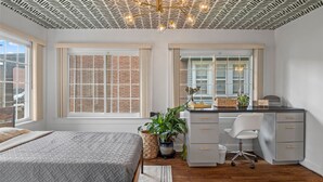 Ein Schlafzimmer mit Bett, Schreibtisch, Stuhl und Zimmerpflanzen.