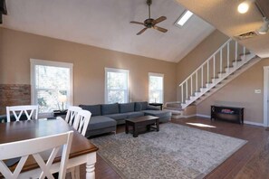 A living room with a sofa, a dining table with chairs, a staircase, and a ceiling fan.