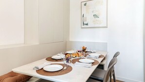 Un coin repas avec une table dressée pour deux personnes, comprenant une table de couleur claire, des sets de table marron et un verre de jus de fruits.