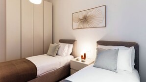 Une chambre avec deux lits, une table de chevet avec une lampe, une armoire et une œuvre d’art encadrée au mur.