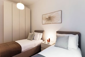 A bedroom with two beds, a nightstand with a lamp, a wardrobe, and a framed artwork on the wall. - The Monti Residence - My Home in Como (Como)