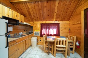 Cocina compacta con muebles de madera, un lavamanos, microondas y comedor con mesa y sillas.