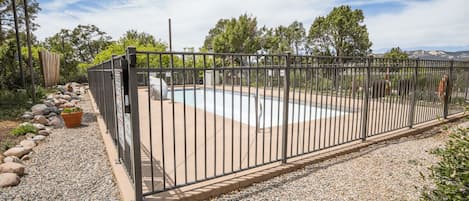 Un área de piscina al aire libre con cerco, un camino de grava y una valla de madera.