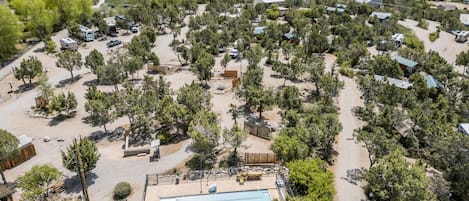 Vue aérienne d’un terrain de camping avec des camping-cars, une piscine et des arbres dispersés.