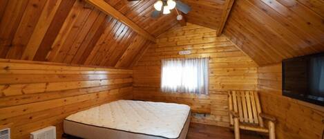 Une chambre dans un chalet en bois, comprenant un lit, un ventilateur de plafond, un radiateur, une fenêtre avec des rideaux et un téléviseur.