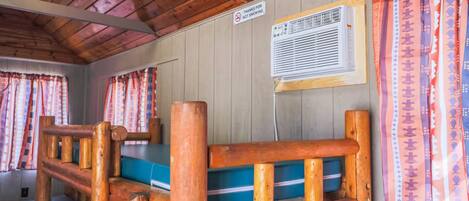 A room with a wooden ceiling, a bed with a blue mattress, a wall-mounted air conditioner, and a 'No Smoking' sign.