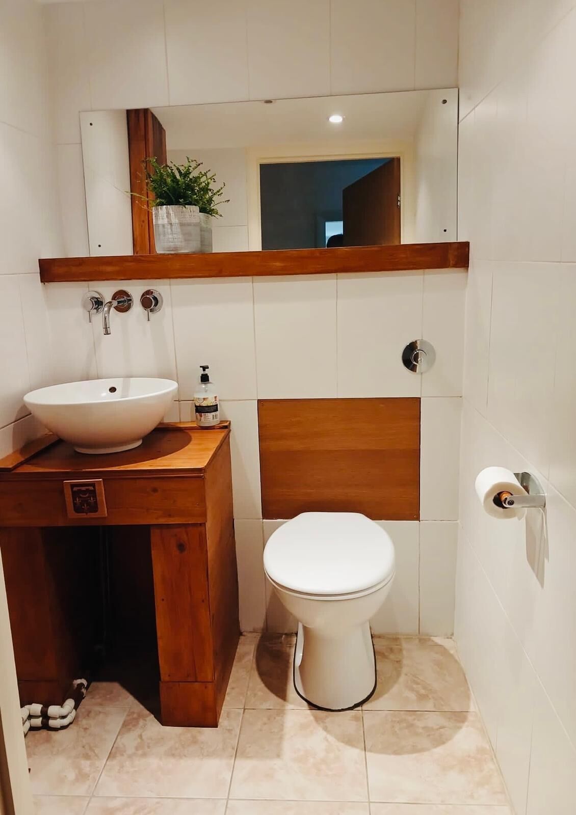 Et badeværelse med en hvid vask, et træbord, et toilet og et spejl over vasken.