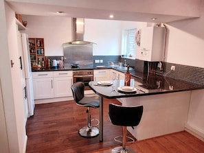 A compact kitchen with a central island, two bar stools, and a dining area. - Cosy Apartment London (London)