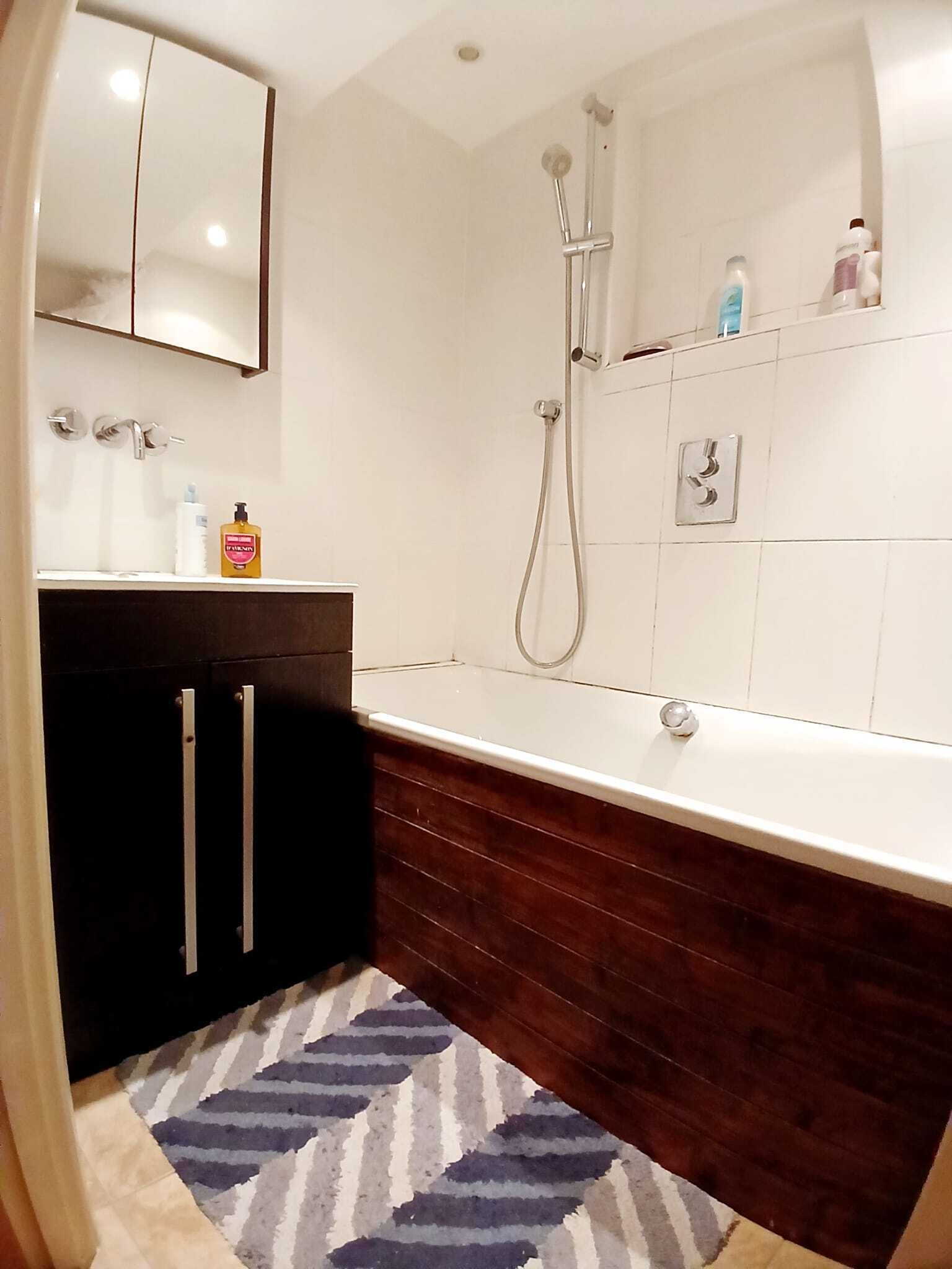 Une salle de bain moderne avec une baignoire, une douche, un meuble-lavabo avec un miroir et un tapis.