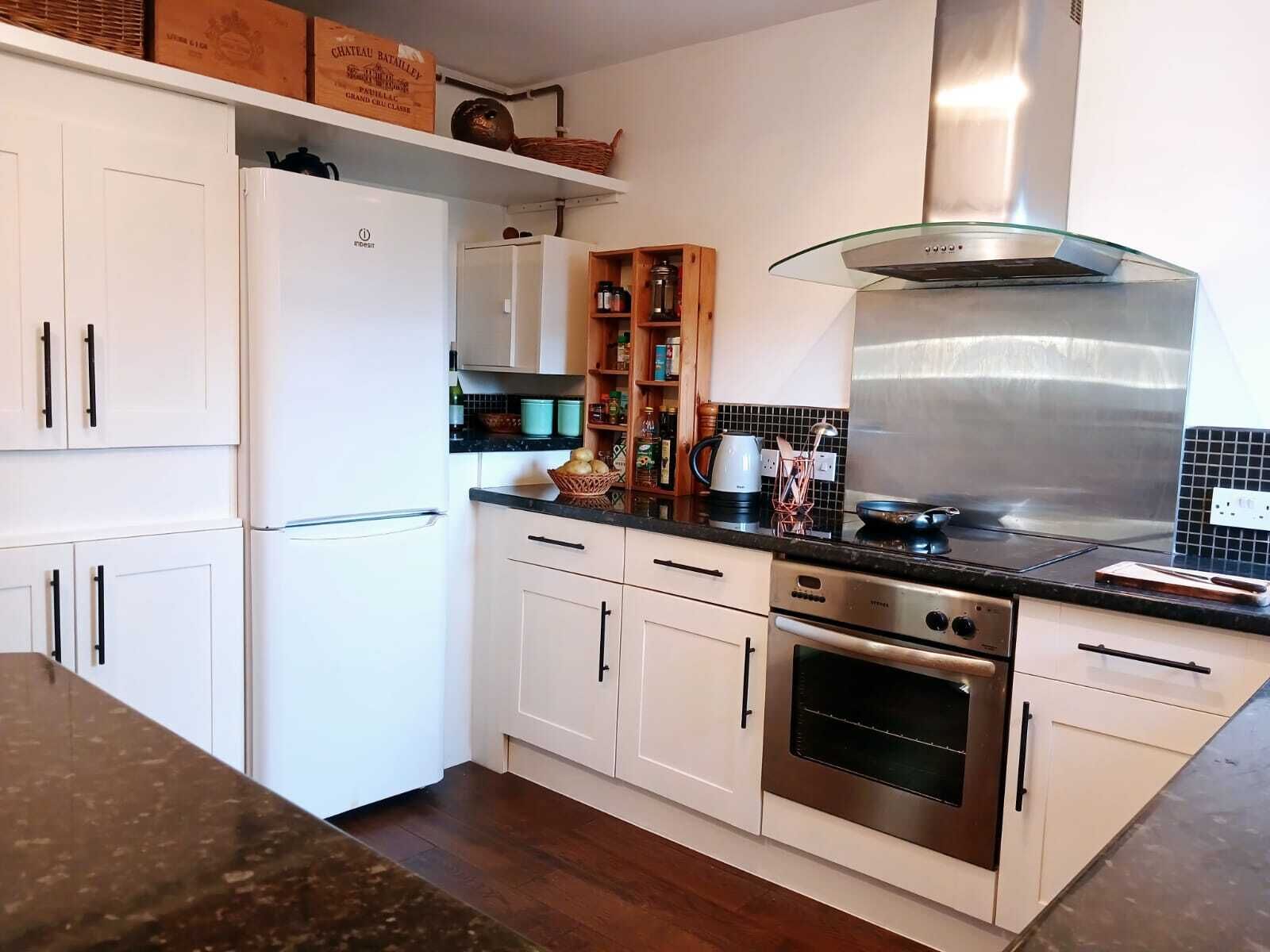 A modern kitchen with white cabinetry, a stainless steel range hood, and a built-in oven.