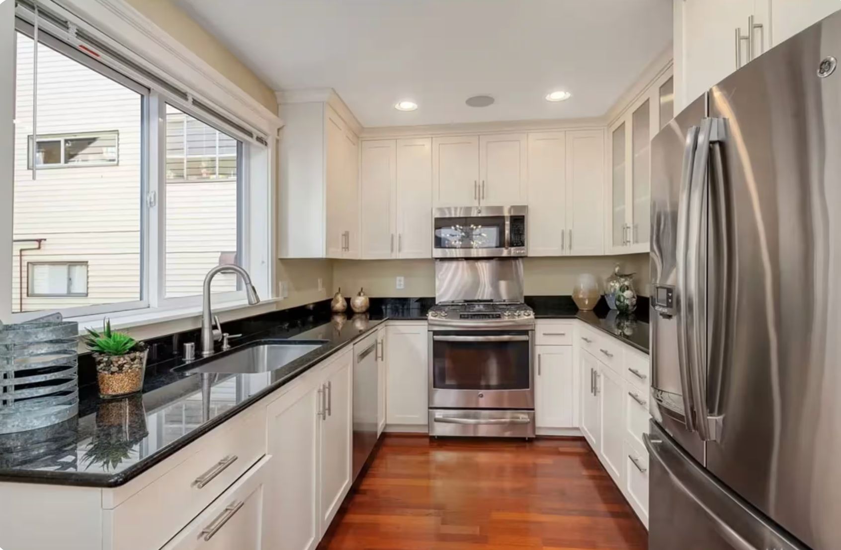 A modern kitchen with stainless steel appliances, white cabinetry, and a black countertop.