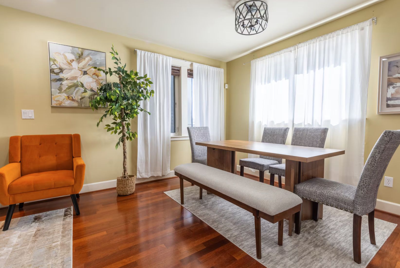 A dining area with a wooden table, grey upholstered chairs, a bench, and a potted plant.
