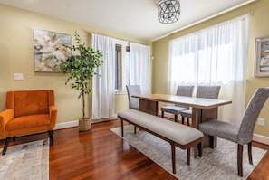 A dining area with a wooden table, grey upholstered chairs, a bench, and a potted plant. - Oceana: Peaceful 5-bedroom Seattle Home 10 mins to DT (Seattle)