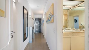 Un couloir avec une porte, un miroir et une salle de bain équipée d’un lavabo et d’un miroir.