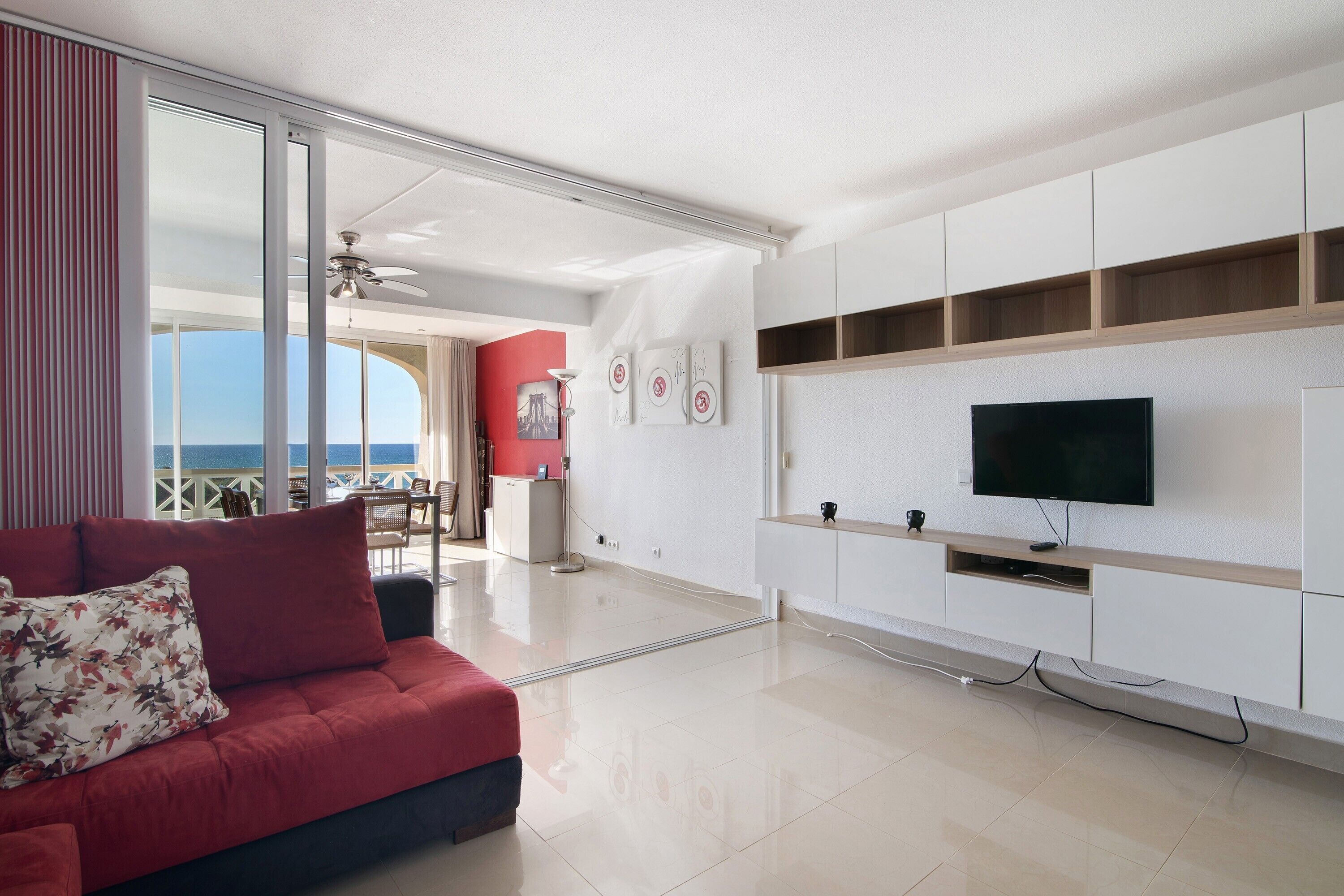 Un salon moderne avec un canapé rouge, un téléviseur à écran plat et un balcon offrant une vue agréable.