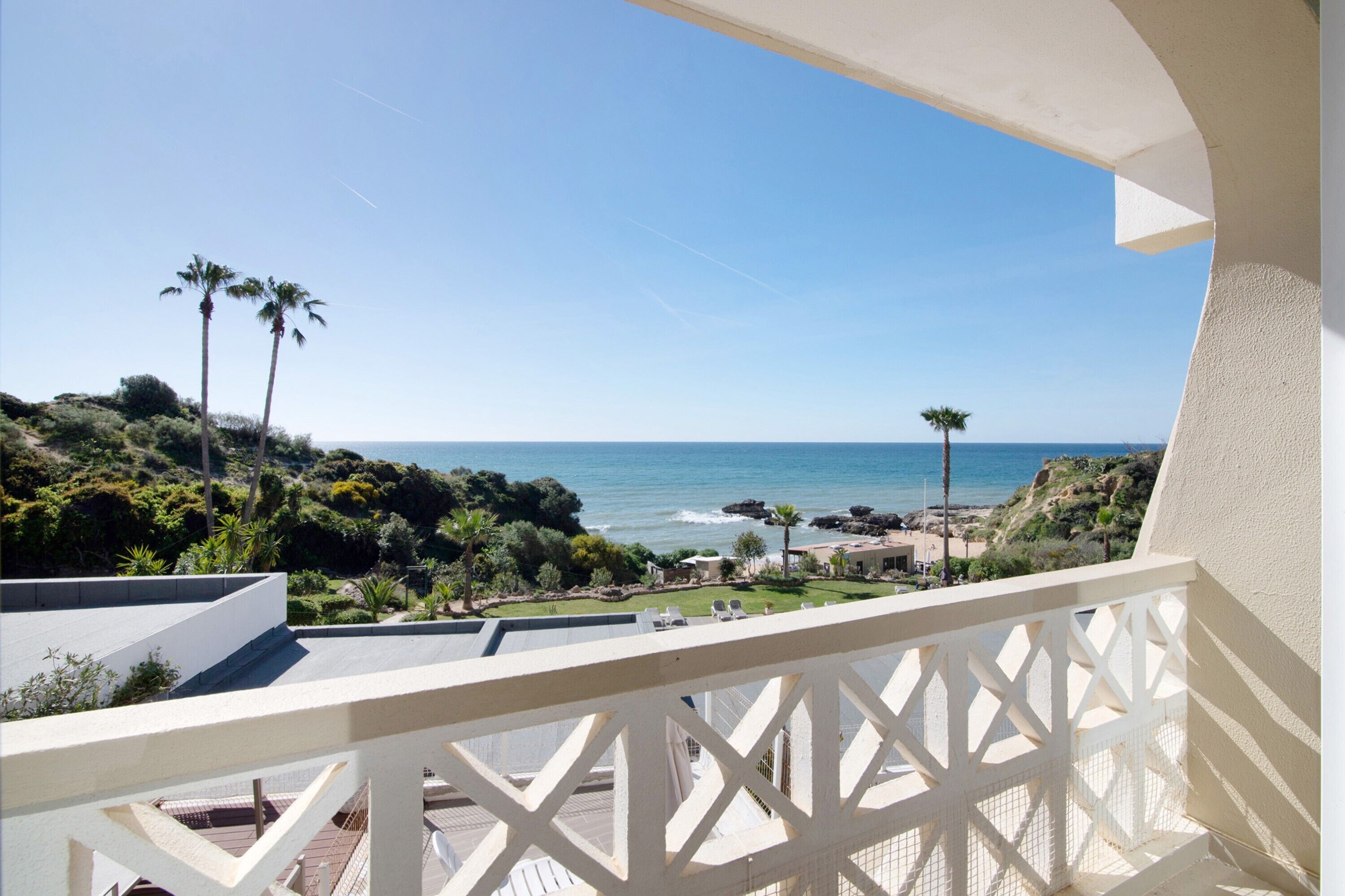 Un balcó amb vista a l'oceà, palmeres i una platja rocosa.