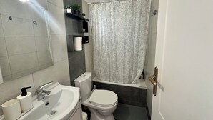 Een badkamer met een wastafel, toilet, douchegordijn en planken met toiletartikelen.
