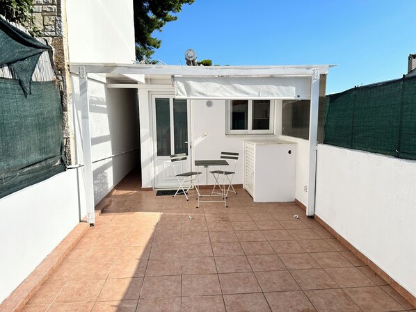 A small patio area with a white table and chairs, a compact refrigerator, and a window overlooking a garden. - Jet lag by the Sea Stylish House close toAthens airport,Rafina port, Ahens (Artemis)