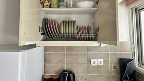 Een keukenkast met afwasspartij, een waterkoker en een raam met zonwering.