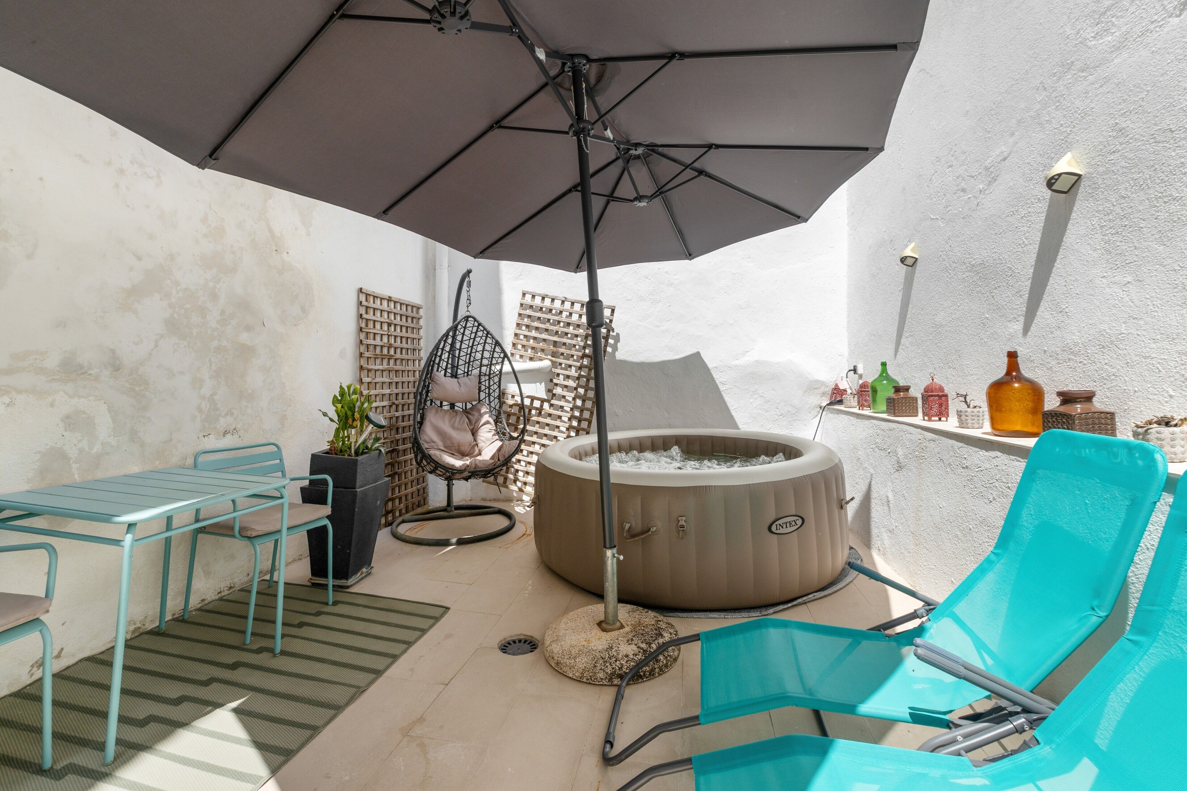 Een terras met een glazen tafel, een hangstoel, een jacuzzi en een loungestoel.