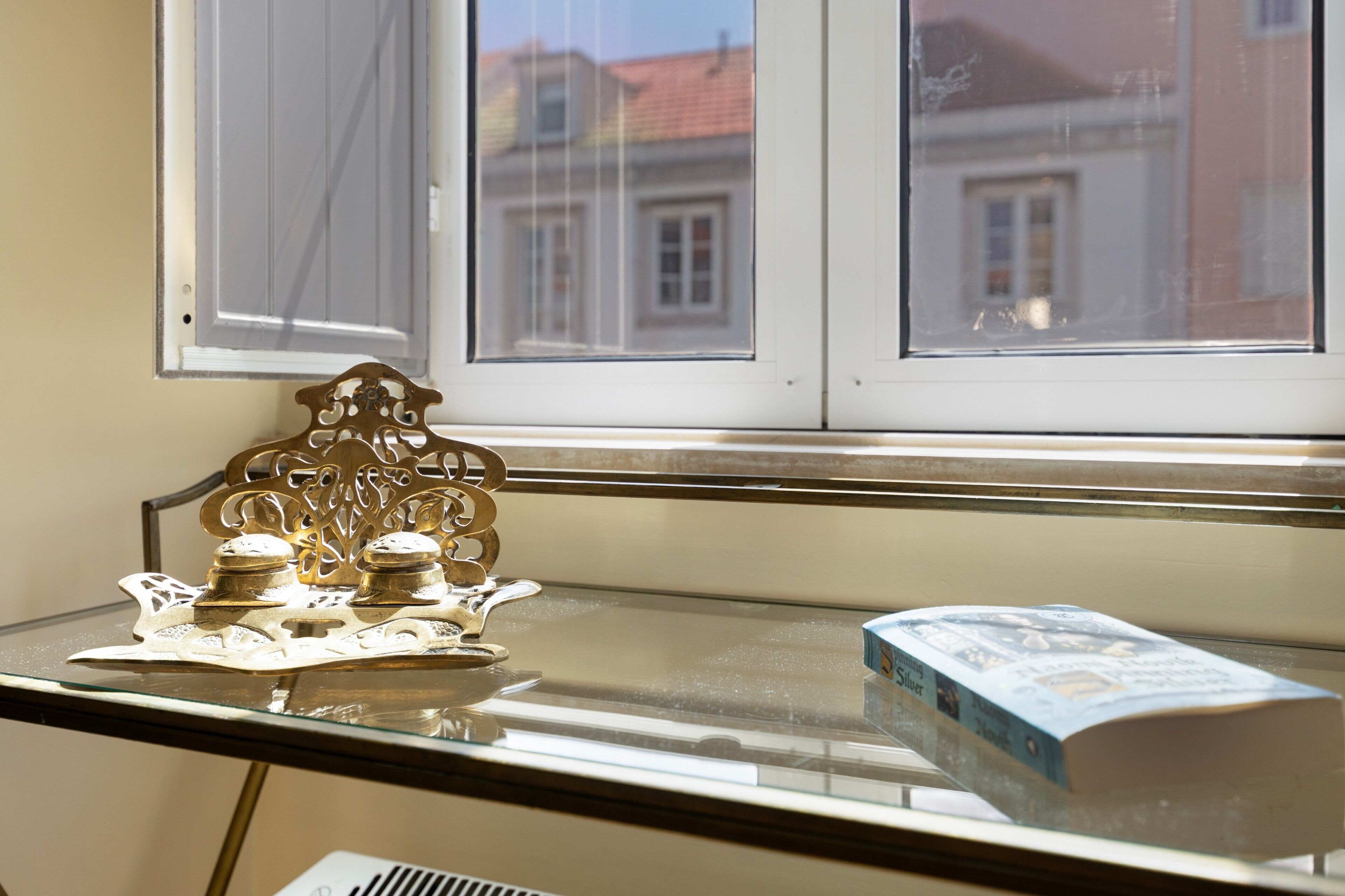 Een raam met uitzicht op gebouwen, een tafel met een decoratief metalen object en een doos.