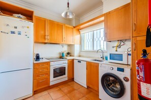 A compact kitchen with wooden cabinets, a built-in oven, a dishwasher, and a washing machine. - Casa Monte Verde in Vilamoura (Vilamoura)