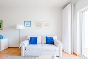 A white sofa with blue cushions, a white side table, a floor lamp, and two framed pictures on the wall. - Casa Monte Verde in Vilamoura (Vilamoura)