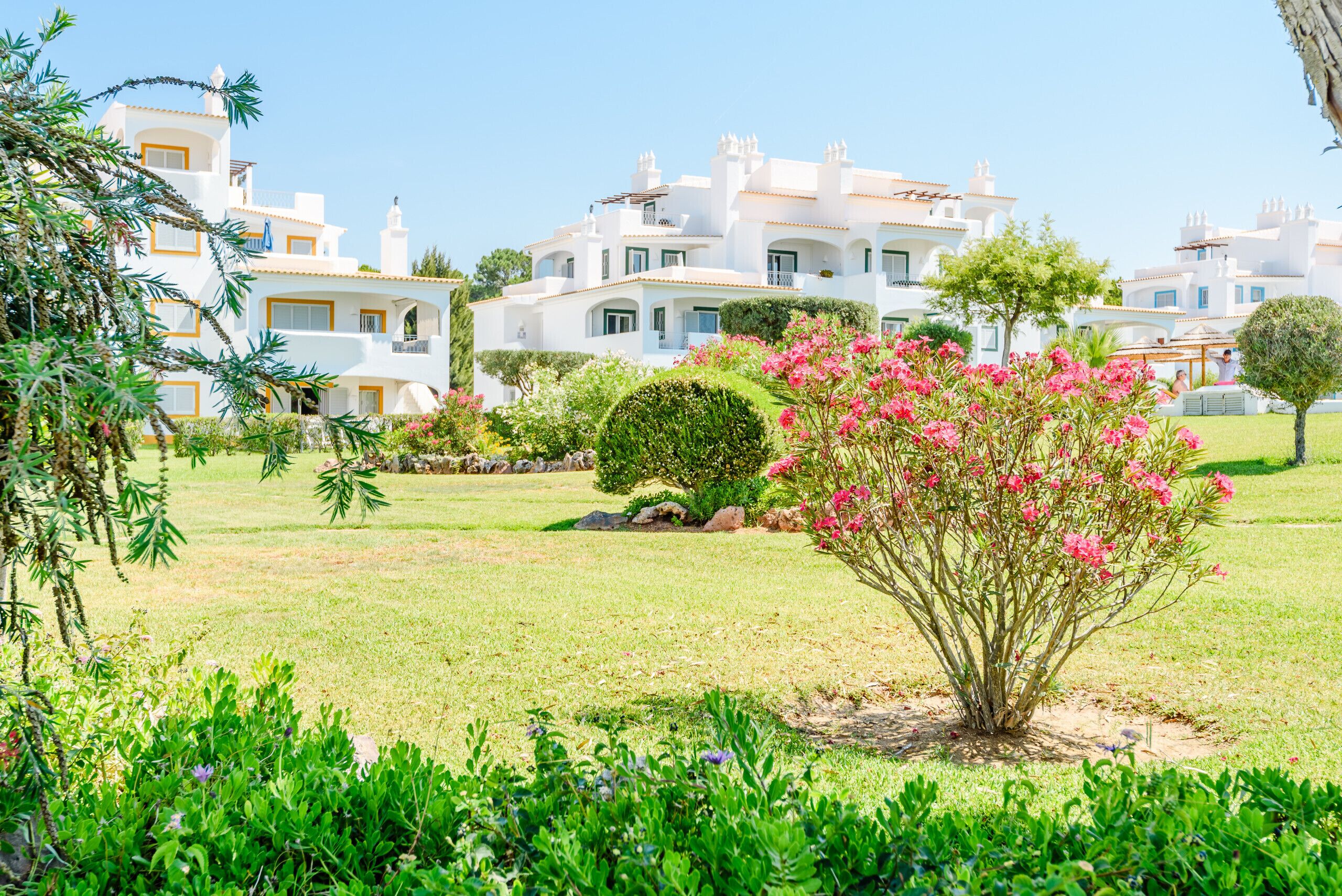 A white building with multiple balconies and a well-maintained garden with pink flowers.