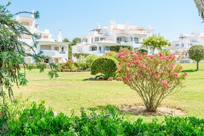 A white building with multiple balconies and a well-maintained garden with pink flowers. - Casa Monte Verde in Vilamoura (Vilamoura)