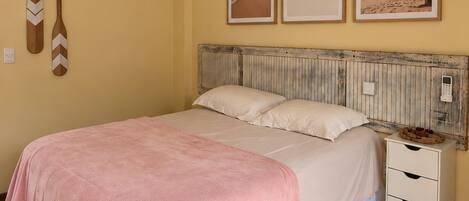 A bedroom with a bed, a nightstand, a wooden floor, and wall-mounted decorations.