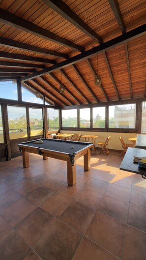 A pool table in a room with large windows and a wooden ceiling. - Vila Artesania (Bombinhas)