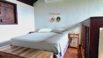 Quarto com cama, mesa de cabeceira e um banco.
