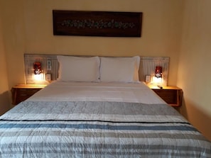Ein Bett mit gestreifter Bettdecke, zwei weiße Kissen und zwei Nachttische mit roten Lampenschirmen.