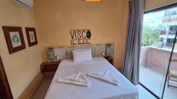 A hotel room with a bed, a sign on the wall, a window, and a view of the outside.