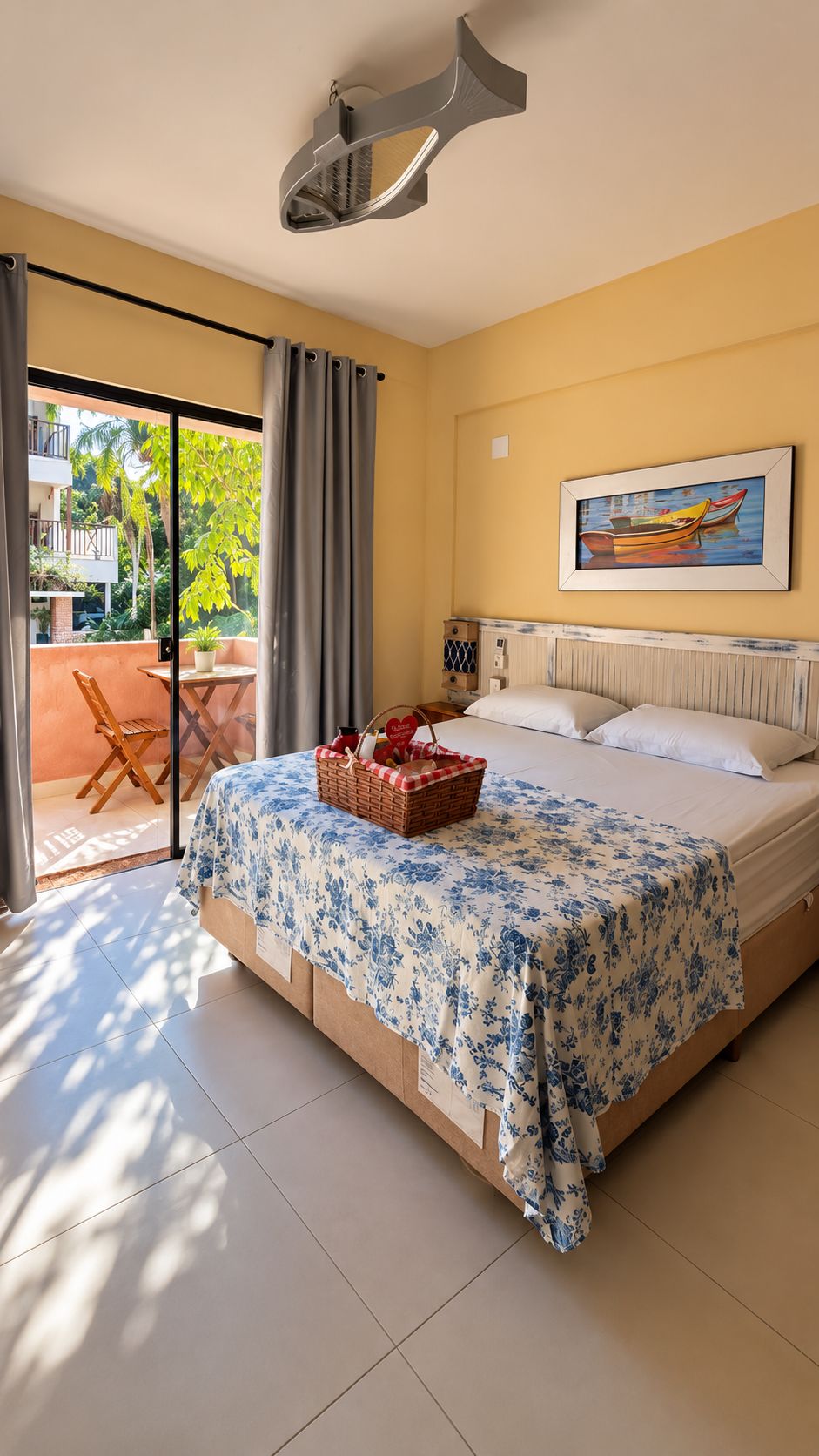 Une chambre avec un lit, une fenêtre donnant sur un paysage verdoyant, un tableau accroché au mur et un panier posé sur le lit.