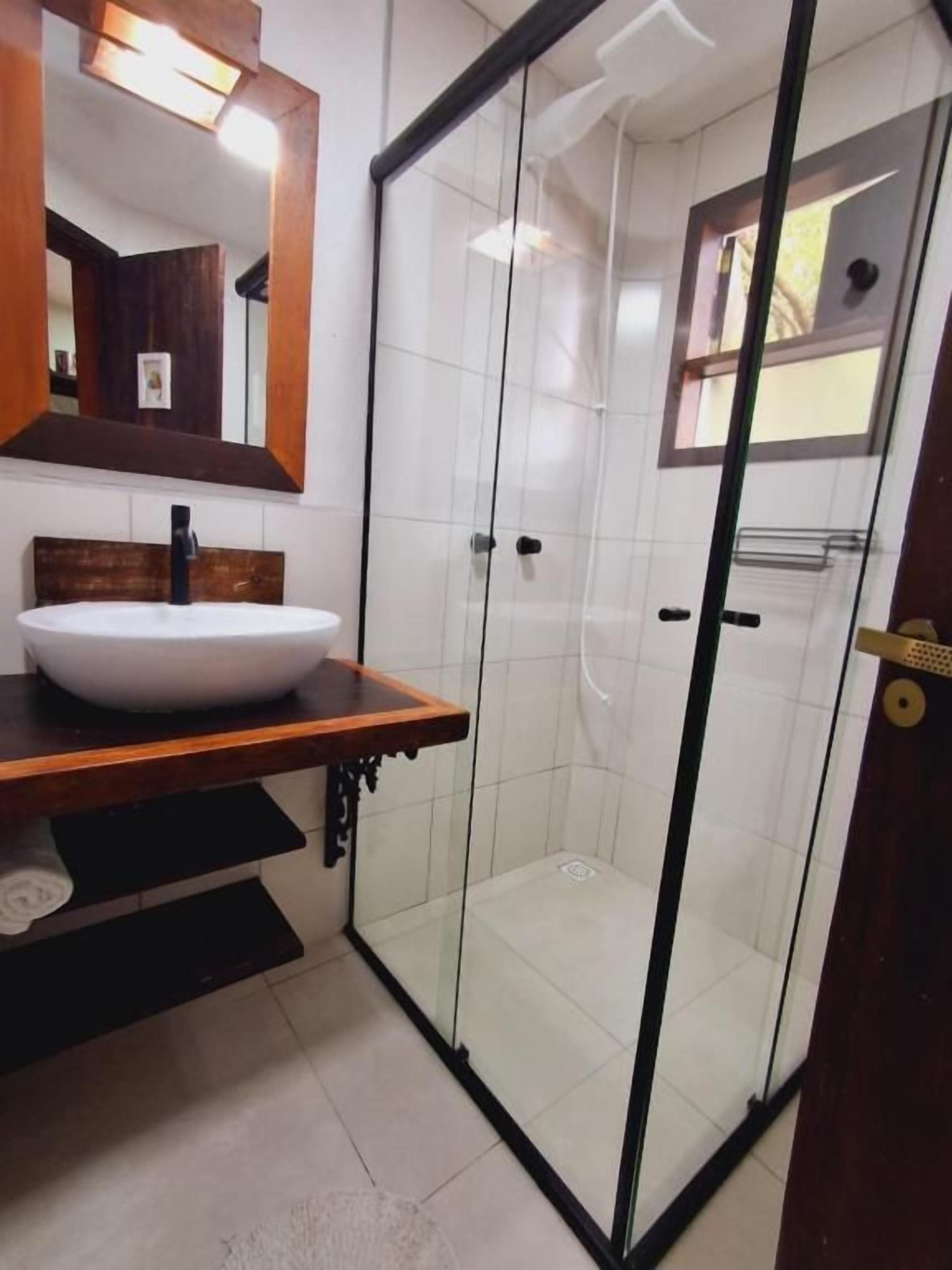 Une salle de bain avec une douche à parois de verre, un meuble-lavabo en bois avec un lavabo blanc et un miroir au-dessus du lavabo.