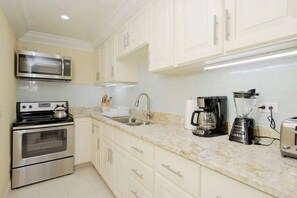 A kitchen with white cabinets, a stainless steel oven, a microwave, a coffee maker, a blender, and a toaster.