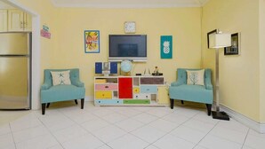 Una sala de estar con televisor, dos sillones, un mueble de colores y un refrigerador.