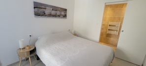 Quarto com cama, mesa de cabeceira com abajur, quadro na parede e porta com porta-toalhas.