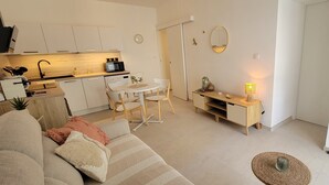 Un espai habitable compacte amb una cuineta, zona de menjador i zona d'estar amb un sofà i una taula petita.