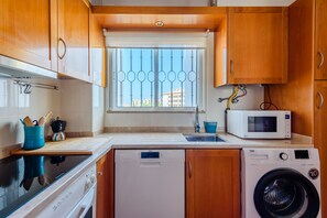 A compact kitchen with wooden cabinets, a built-in dishwasher, a microwave, and a washing machine. - Casa Monteverde (Loulé)