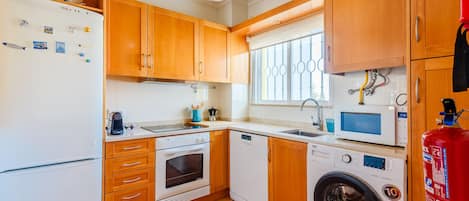 A compact kitchen with wooden cabinets, a built-in oven, a dishwasher, and a washing machine.
