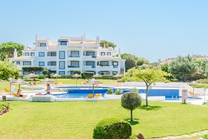 Ein großes, weißes Gebäude mit mehreren Balkonen, einem Swimmingpool und Liegestühlen.