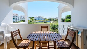 Varanda com mesa e cadeiras de madeira, com vista para uma piscina e edifícios.